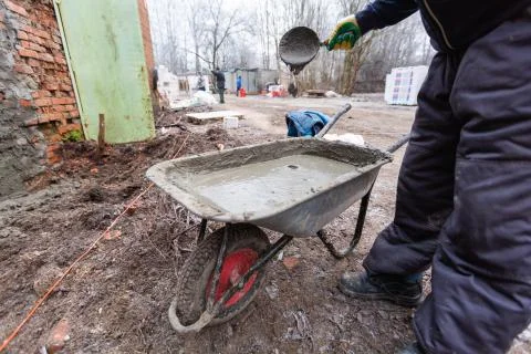 Worker in protect gloves is mixing up the liquid cement in construction trolley Stock Photos