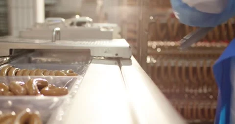 Worker in protective clothing placing fresh sausages into plastic trays on a Stock Footage 339984335