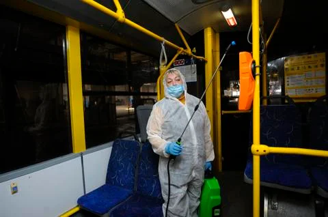 Worker in protective face mask and costume disinfecting the trolleybus interi Stock Photos