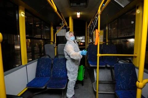 Worker in protective face mask and costume disinfecting the trolleybus interi Stock Photos