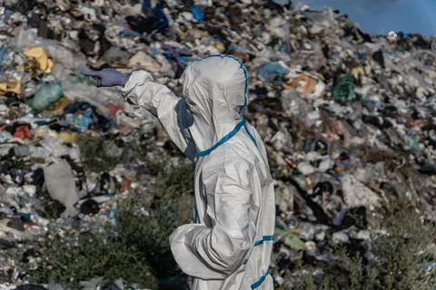 A worker in protective gear inspects a large landfill site filled with garb.. Stock Photos