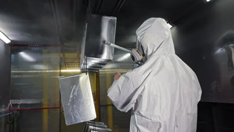 Worker in protective gear spraying powder coating on hanging metal panels Stock Footage 309231682