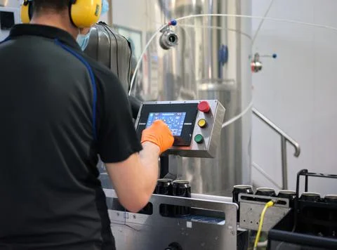 Worker with protective gear using an electronic device of a machine in a brewery Stock Photos