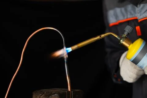 A worker in protective gloves brazing a copper pipe with a gas torch Stock Photos