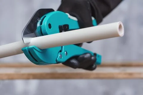 Worker in protective gloves cutting a PVC pipe with a turquoise manual pipe c Stock Photos