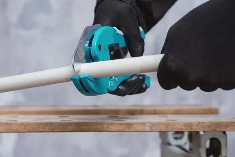 Worker in protective gloves cutting a PVC pipe with a turquoise manual pipe c Stock Photos