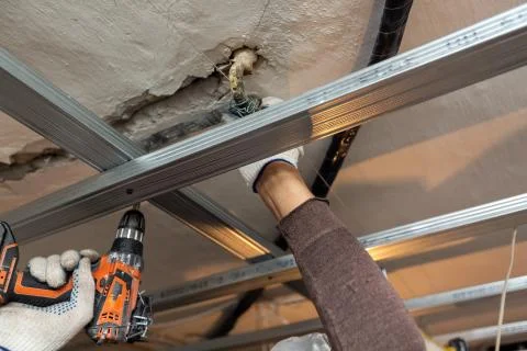 Worker with protective gloves is drilling by perforator the ceiling for Stock Photos