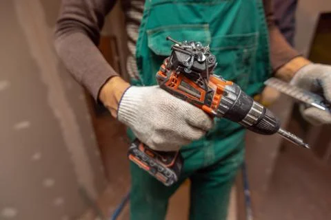Worker with protective gloves is holdind a drill in apartment that is under Stock Photos