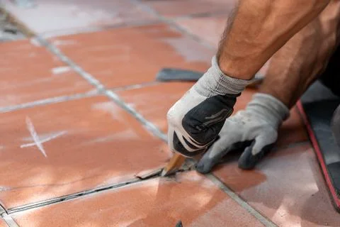 Worker in protective gloves pries up damaged floor tiles with a chisel during Fotos Stock