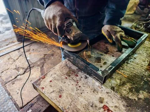 Worker in protective gloves using an angle grinder to grind a metal frame 스톡 사진