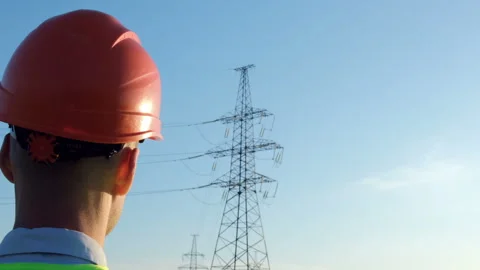 Worker in a protective helmet against the background of a high-voltage line Stock Footage 137455173