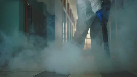 Worker in protective suit disinfecting corridor with smoke machine cold fog.. Stock Footage 337539266