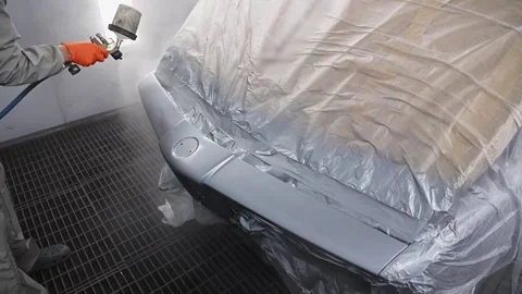Worker in a protective suit with a mask paints car parts in a special enclosed Stock Footage 259243432