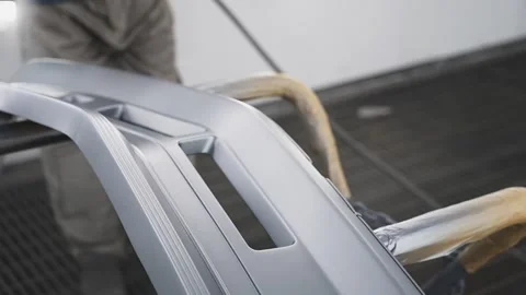 Worker in a protective suit with a mask paints car parts in a special enclosed Stock Footage 259641538
