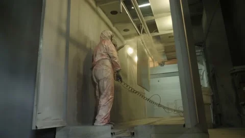 Worker in protective suit sprays powder paint from gun on metal products Stock Footage 150746085
