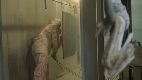 Worker in protective suit sprays powder paint from gun on metal products Stock Footage 150778478