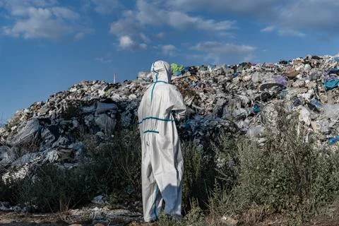 A worker in a protective suit studies a massive pile of garbage at a landfi.. Stockfoto's