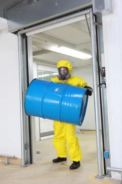 Worker in protective uniform lifting barrel of toxic substance Stock Photos