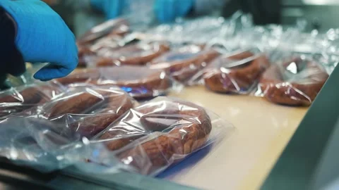 Worker in protective uniform pack and stack sausages in plastic packaging Video stock 241010099