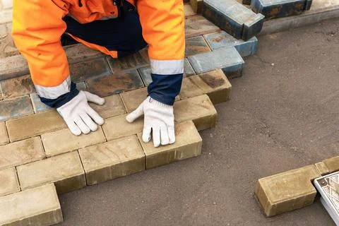 A worker in a protective work suit lays paving slabs. A professional Stock Photos