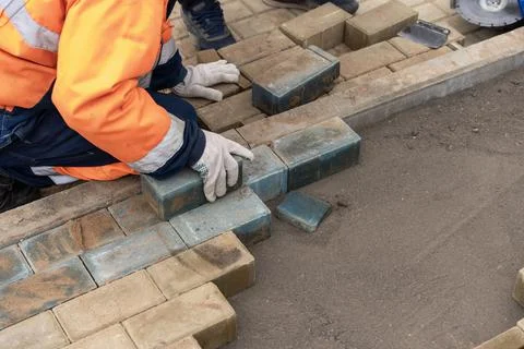 A worker in a protective work suit lays paving slabs. A professional Foto stock