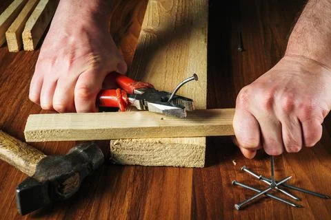 The worker pulls the bent nail out of the board with pliers. Woodworker hands Stock Photos