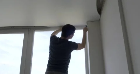 Worker pulls ceiling fabric, tuck ends of matte fabric into fixtures with trowel Stock Footage 130781381