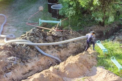 Worker pulls a flexible pipe along the trench. Stock Photos