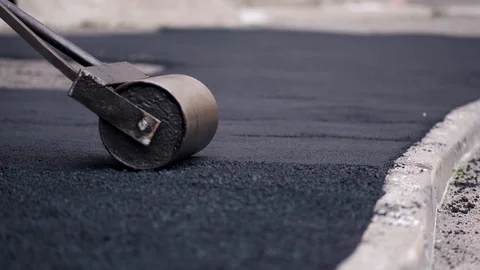 The worker pushes a manual roller for asphalt paving of the sidewalk. Stock Footage 124904033