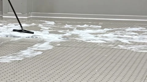 Worker pushes thick cleaning foam across tiled flooring with a floor squeegee Stock Footage 326281956