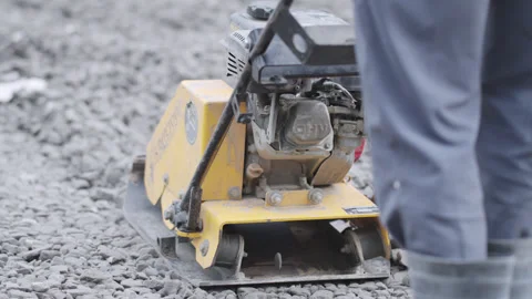 Worker pushes vibratory plate across gravel covered surface 動画素材 329866918