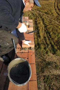 The worker puts the brick on the cement mortar on the background of the grass Stock Photos