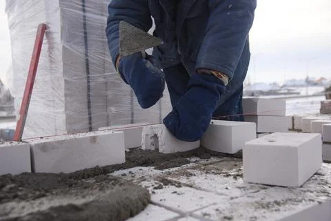 A worker puts bricks in cement in straight rows, laying concrete blocks. Stock Photos