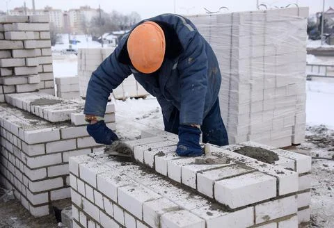 A worker puts bricks in cement in straight rows, makes a concrete wall. Stock Photos
