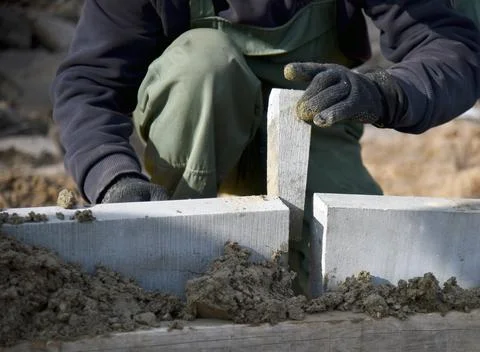 A worker puts a concrete wedge between two concrete curbs. Stock Photos