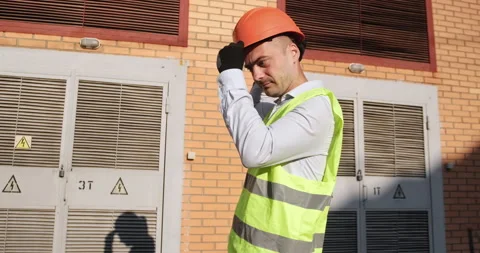 Worker puts on orange helmet standing by electric substation Vidéo 160818296