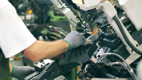 A worker is putting a shoe into a machine which is shaping it. Factory Video stock 140564437