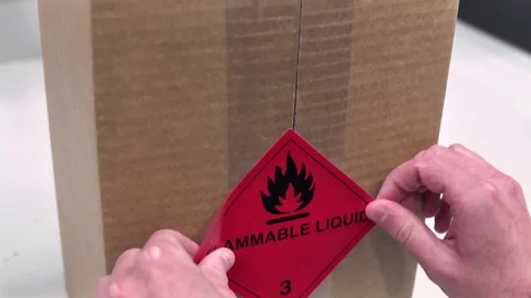 Worker putting a sticky label reading flammable liquid on a cardboard box Stock Footage 113332296