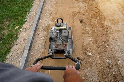 Worker rams the ground with a vibrating machine. Top view. Stock Photos