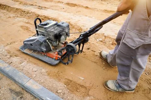 Worker rams the ground with a vibrating machine. Stock Photos