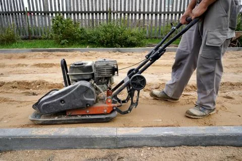 Worker rams the ground with a vibrating machine.Side view. Stock Photos