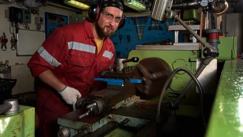Worker in red uniform operating in manual lathe in metal big workshop with da Stock Photos