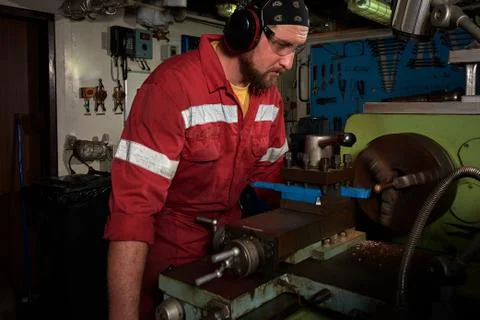 Worker in red uniform operating in manual lathe in metal big workshop with da Stock Photos