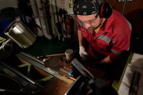 Worker in red uniform operating in manual lathe in metal big workshop with da Stock Photos