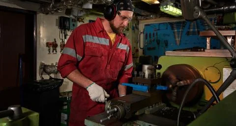 Worker in red uniform operating in manual lathe in metal big workshop with da Stock Photos