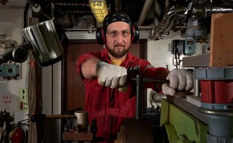 Worker in red uniform operating in manual lathe in metal big workshop with da Stock Photos