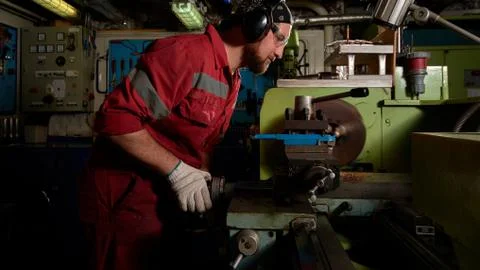 Worker in red uniform operating in manual lathe in metal big workshop with da Foto stock