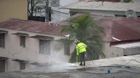 Worker in reflective jacket uses pressure washer to clean a rooftop Stock Footage 343882935