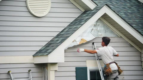 A worker removes old siding panels outside walls of the private house Видео 327163925