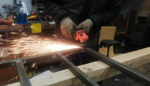 A worker removes rust from metal using a grinder and a grinding stone, sparks Stock Photos